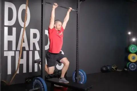 Man performing a hanging exercise, possibly part of butterfly sets, in a gym.