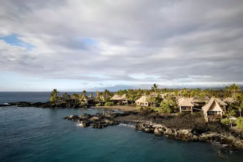 Tropical bungalows on a rocky coast in Kona, Hawaii. The calm ocean reflects the cloudy sky, a stark contrast to the power of a tsunami.