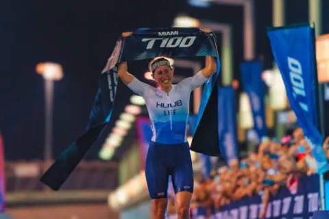 India Lee celebrates a victory, holding up a "Miami T100 World Tour" banner.