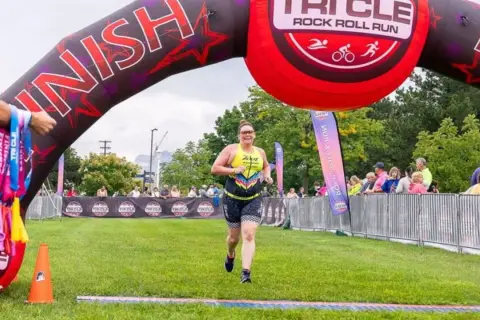 A woman crosses the finish line at a triathlon, smiling. This event is one of the best triathlons for participants to achieve their goals.