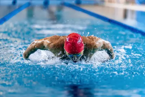 A swimmer in a red cap and goggles powers through the water, showcasing the strength and full-body engagement of breaststroke benefits.