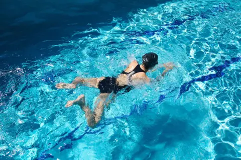 Swimmer in black suit performing breaststroke, showing the characteristic bent leg position of the breaststrokers knee.