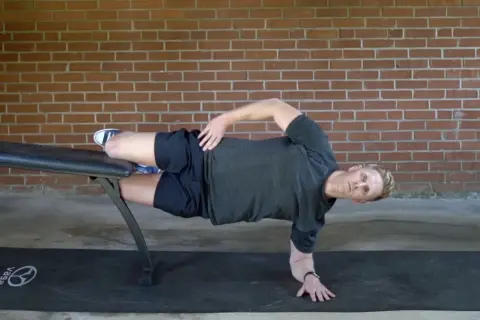 Man performing a side plank on a bench, a key exercise for core workouts for swimmers.