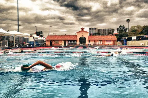 Swimmers race in an outdoor pool under a dramatic cloudy sky, enjoying a refreshing morning swim.