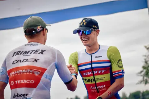 Gustav Iden, a triumphant triathlete, shares a handshake after a race, his smile wide and his racing suit vibrant.
