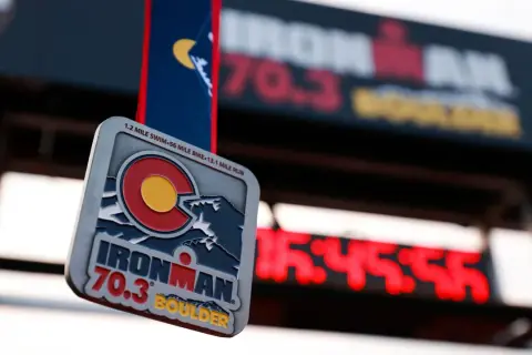Ironman 70.3 Boulder medal hangs in front of a finish line clock. The medal features the Colorado flag and mountains.
