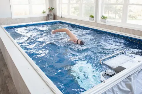 Man swims laps in a compact triathlon pool, enjoying an endless swim against a gentle current.