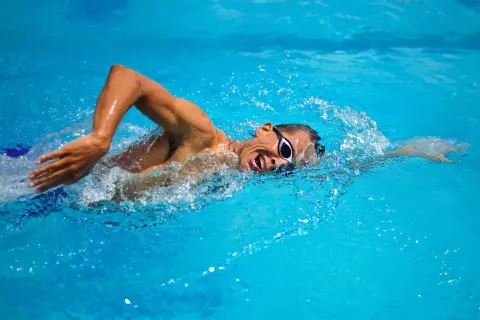 Swimmer with goggles in bright blue water, performing bilateral breathing during a freestyle stroke.