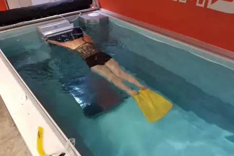 Woman with yellow fins practicing her leg kicking in a swim spa.