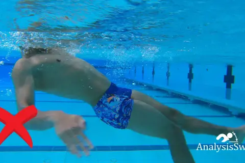 Underwater view of a swimmer demonstrating an incorrect backstroke arm movement. A red X marks the improper arm position.
