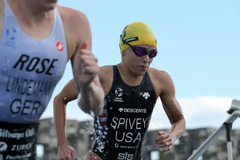 Taylor Spivey, a triathlete in a yellow cap and goggles, emerges from the water, her USA suit glistening.