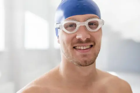 A smiling man in a blue swim cap and goggles, ready to swim. He's wondering, "When can I swim after wisdom teeth removal?