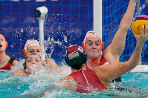 Intense water polo action, with players battling for the ball. The struggle suggests potential water polo fouls as they jostle for position near the goal.