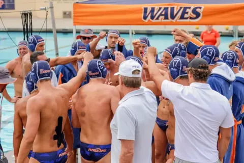 Waterpolo development: A team huddles, fists raised, showing unity and focus before a game.