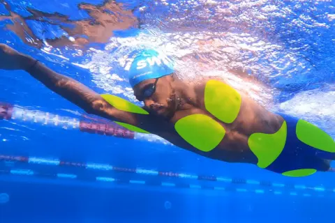A swimmer's body, with neon green highlights on their torso and arms, glides through a blue pool.