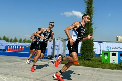 Athletes in racing gear push forward during a triathlon training run, focused and determined under a bright blue sky.