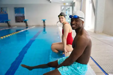 Smiling adults in swim gear at pool edge, ready for swim lessons for adults with fear of water.