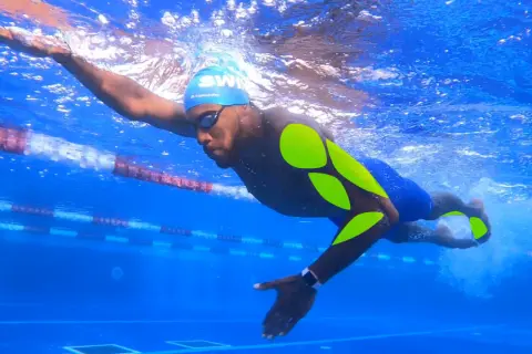 Swimmer in blue cap and goggles, with neon green markings on his body, powerfully pulls through the water in a lane.