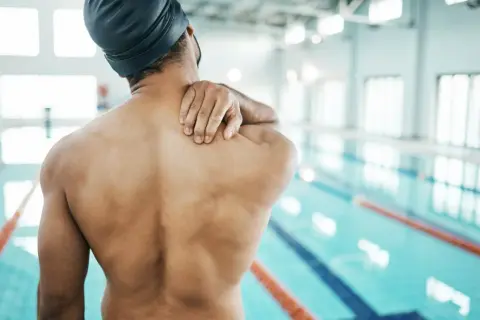 Swimmer holding shoulder in pain, questioning if you can swim with a torn rotator cuff.
