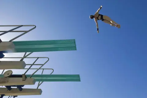 A diver in mid-air, performing a competitive dive against a clear blue sky.