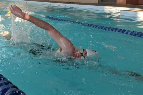 Swimmer pushing hard in a pool, arms extended, water splashing. This intense effort is part of a challenging vo2 max workout.