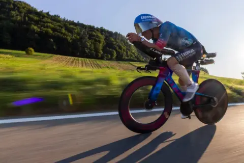 A cyclist in an iron man race powers through a scenic countryside, the blur of motion highlighting their intense effort.