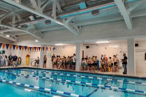 Children in swimsuits gather by the pool at Jim Montgomery Swim School, ready for lessons.