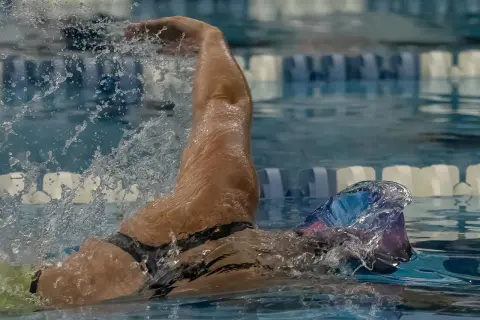 A swimmer's arm slices through the water, demonstrating the powerful stroke needed to swim laps. Water splashes around them as they focus on their technique.