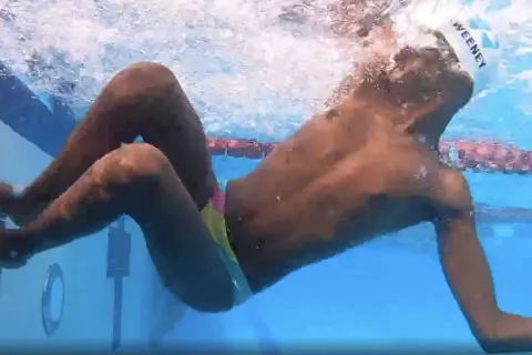 Underwater view of a swimmer performing a breast stroke, with arms extended forward and legs bent, showing the technique.