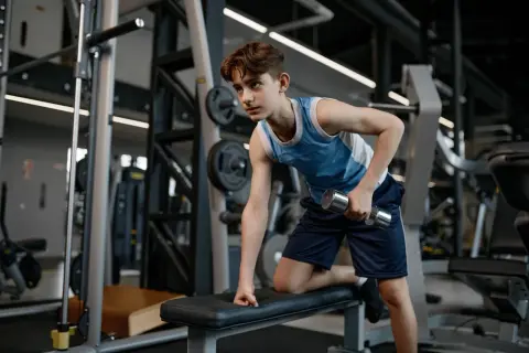 Young swimmer performing dumbbell rows as part of their cross training routine in a gym.