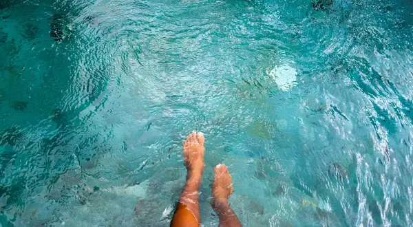Feet submerged in clear turquoise water, with small fish swimming around. A person wonders if they can swim with a yeast infection.