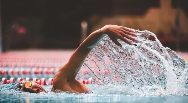 A swimmer's arm slices through the water, creating a dramatic splash during a powerful stroke. The focus is on the dynamic movement as they swim.