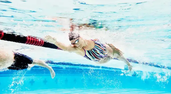 A swimmer in a colorful suit glides through the water, her arm extended, during a recovery swim workout.