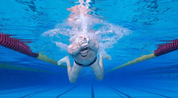 Underwater view of a man performing the breast stroke in a swimming pool, with lane lines and buoys visible.