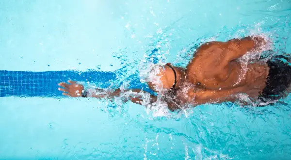 A swimmer powers through the water, creating splashes. This image inspires questions about how long to swim for exercise.