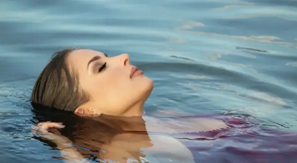 A woman with a new ear piercing floats serenely in the water, her face tilted upwards. She looks relaxed, as if enjoying a peaceful moment, and one might wonder if she can swim after getting ears pierced.