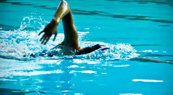 Swimmer's arm in a powerful high elbow catch, slicing through the turquoise water with a splash.