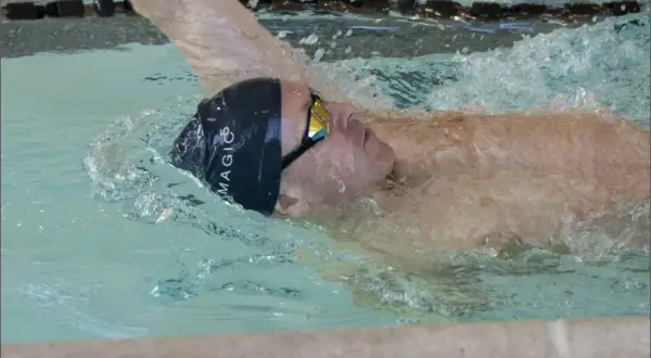 Swimmer executing a backstroke flip turn, water splashing around their head and goggles.