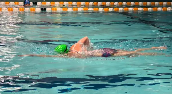 A swimmer in a green cap performs a front crawl swim, their body streamlined as they glide through the turquoise water.