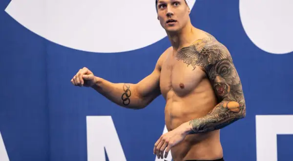 A muscular swimmer with extensive tattoos, including Olympic rings, prepares for a race, showcasing his dedication to swim conditioning.