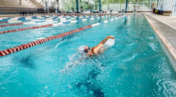 A woman enjoys a 30-minute pool workout, swimming laps in a bright blue lane.