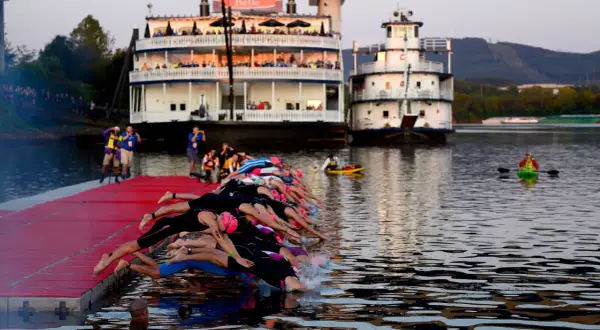 Triathletes dive into the water at 70.3 Chattanooga, with paddle boats and riverboats in the background.