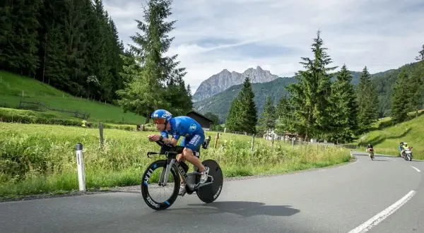 Athlete in blue cycling gear races on a road bike during a sprint triathlon, with a scenic mountain backdrop.