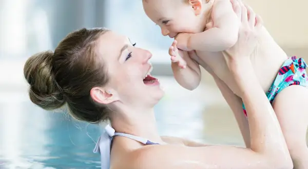 Mother and baby laughing in a pool. A happy mom asks, "When can you swim after C-section?