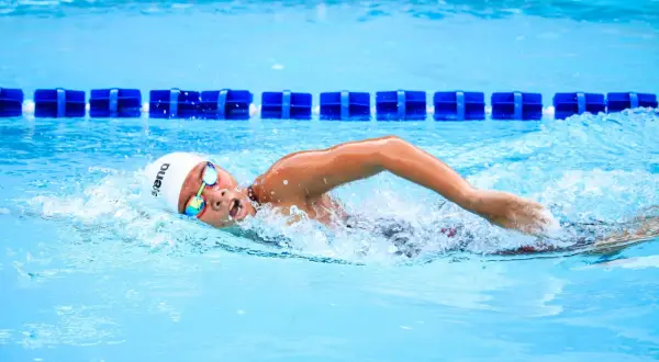 Swimmer in a white cap and goggles executes a powerful american crawl stroke, churning the bright blue water.