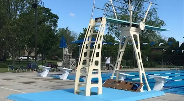A tall, cream-colored high diving board stands ready for action next to a bright blue pool.