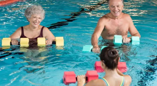 Smiling seniors and a younger woman enjoy water aerobics with buoyant dumbbells. A perfect before and after workout for all ages.