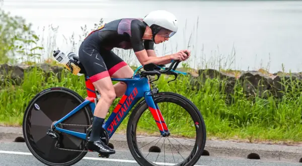 Athlete in a road triathlon, focused and aerodynamic on a blue and red Specialized bike, with a lake in the background.