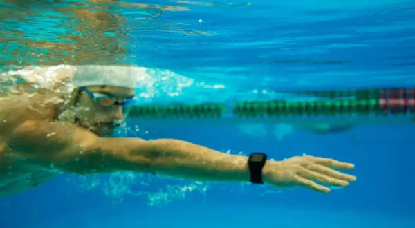 Underwater view of a swimmer in goggles and cap, focused on a long distance swim, with a smartwatch on their wrist tracking progress.