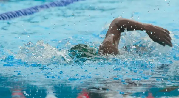 A swimmer powers through the water, mid-stroke, during an intense 1 hour swim workout. Splashes and bubbles fly.
